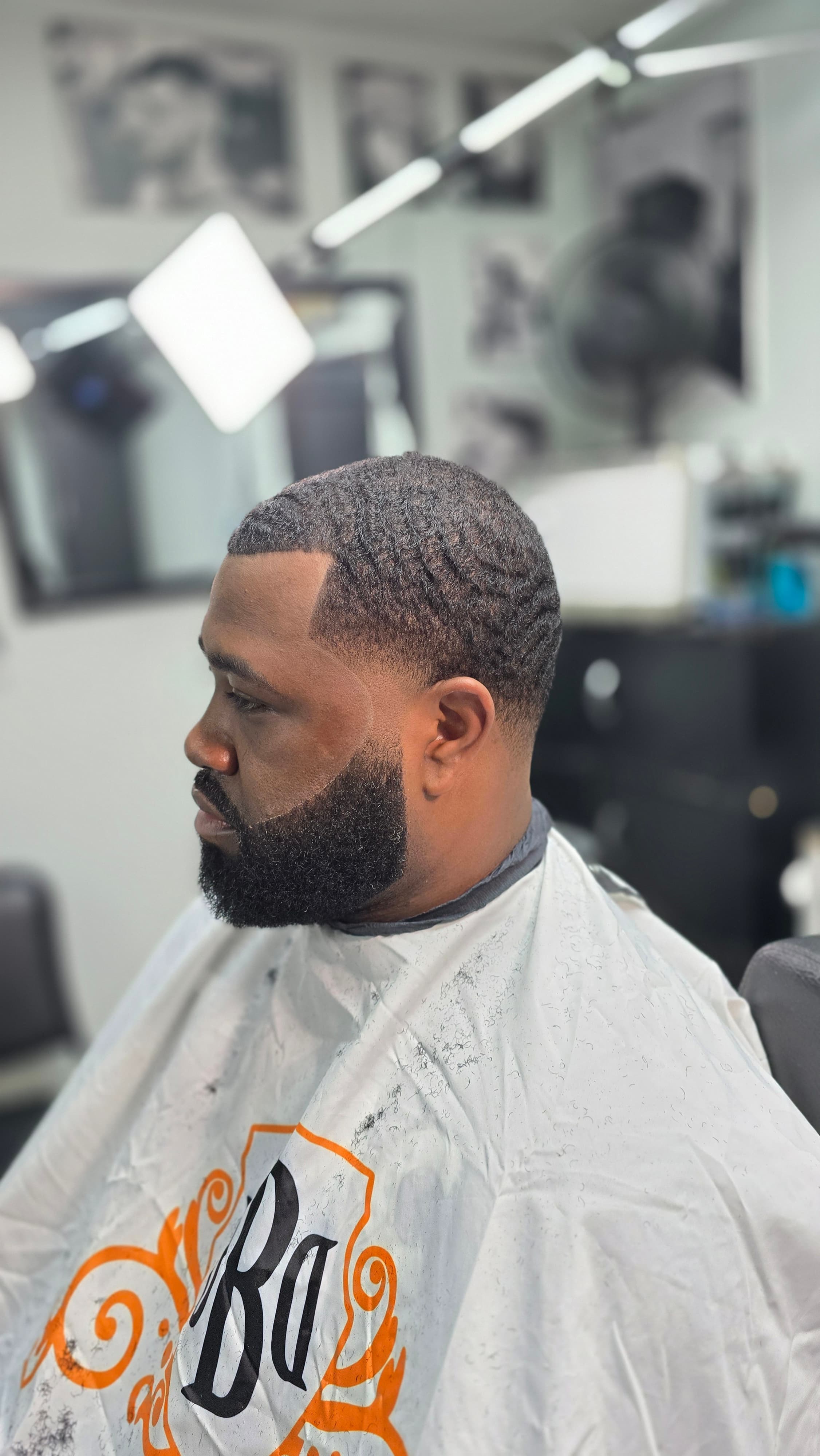 Man with fresh waves and a sharp beard line-up wearing a white barber cape.